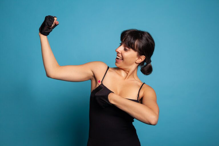 Portrait of athletic fit woman in sportwear showing am muscles after finishing fitness workout in studio with blue background. Personal trainer working at healthy lifestyle practicing sport