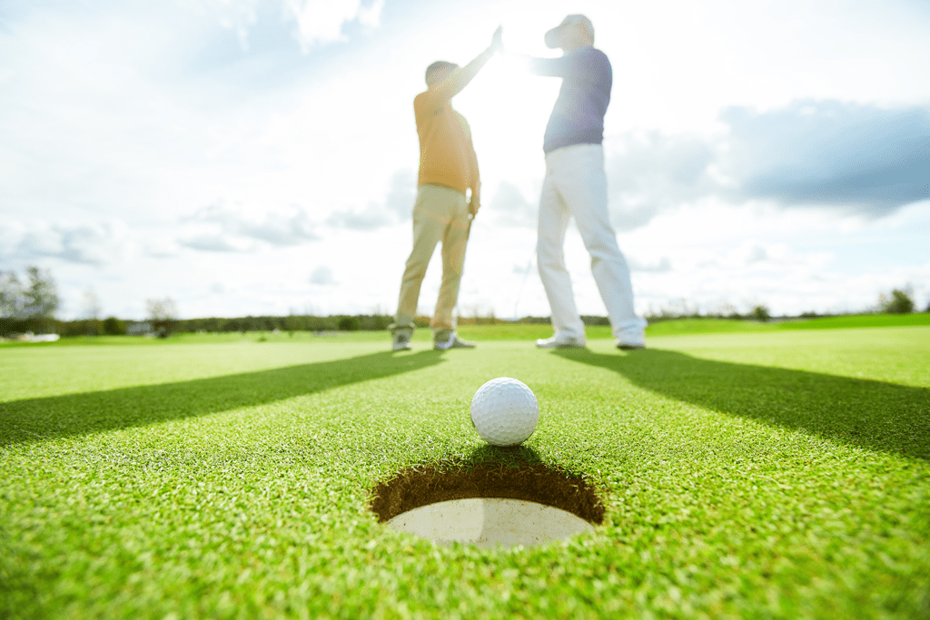 golfers high five near the hole on a sunny day