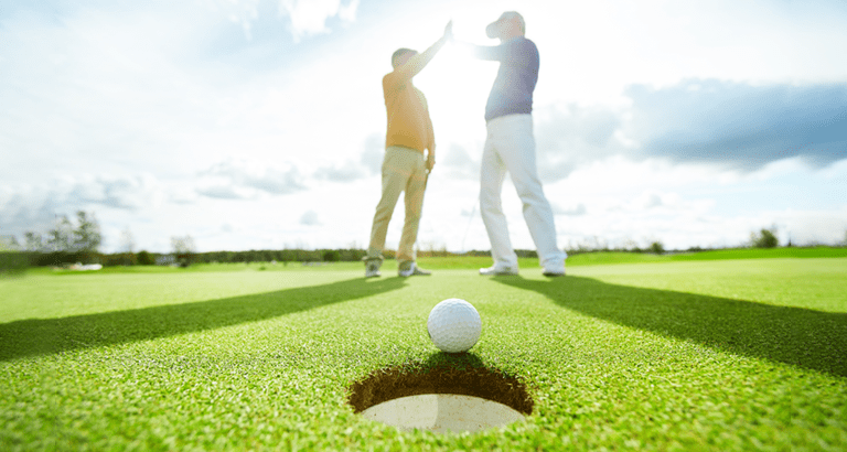 golfers high five near the hole on a sunny day