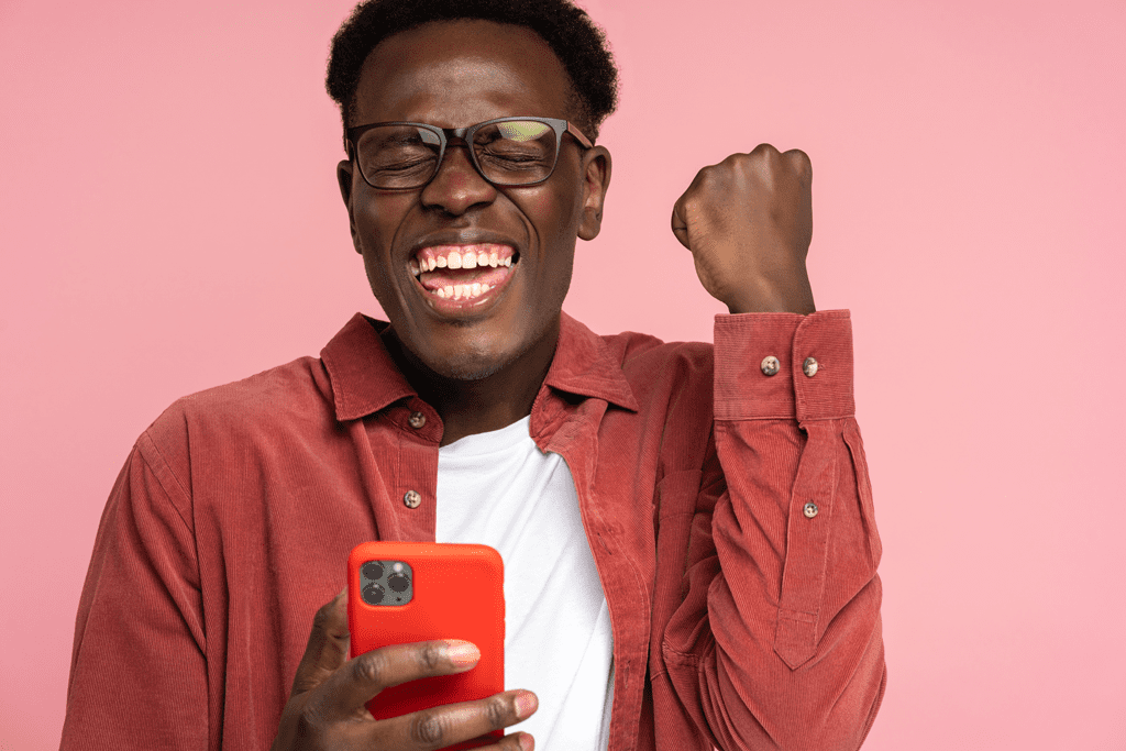 smiling man holding smartphone pumps fist in excitement
