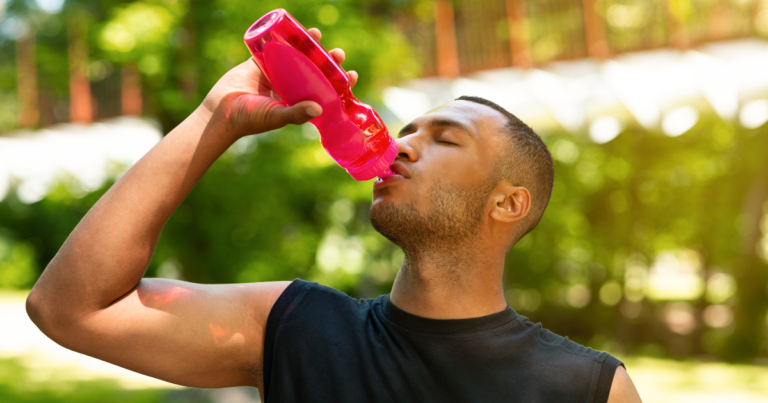 man drinking water from red sports bottle after sweaty workout
